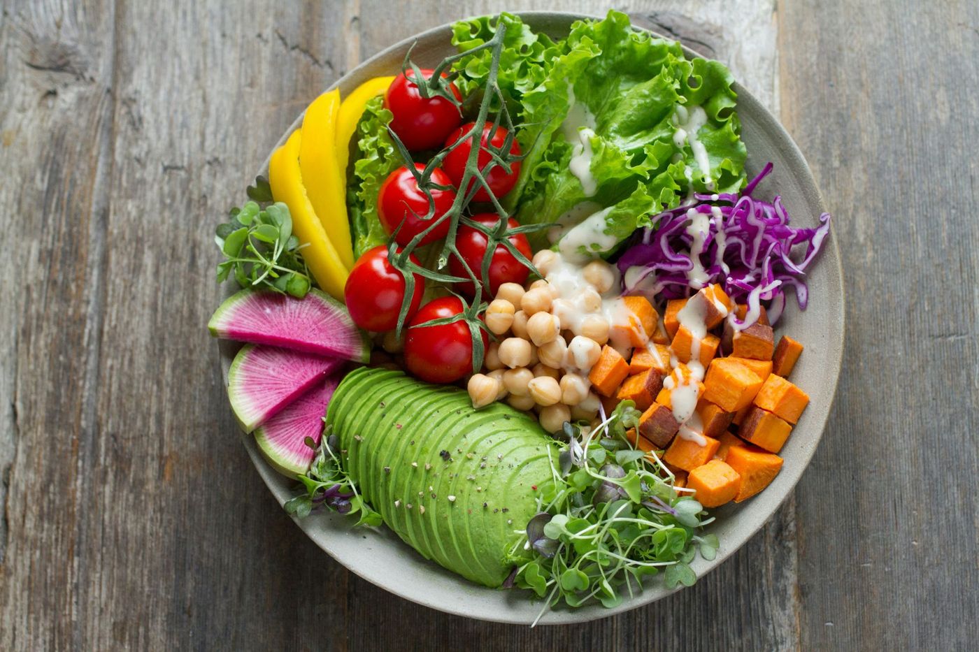 Colorful bowl of greens, tomatoes, chickpeas, sweet potato and avocado